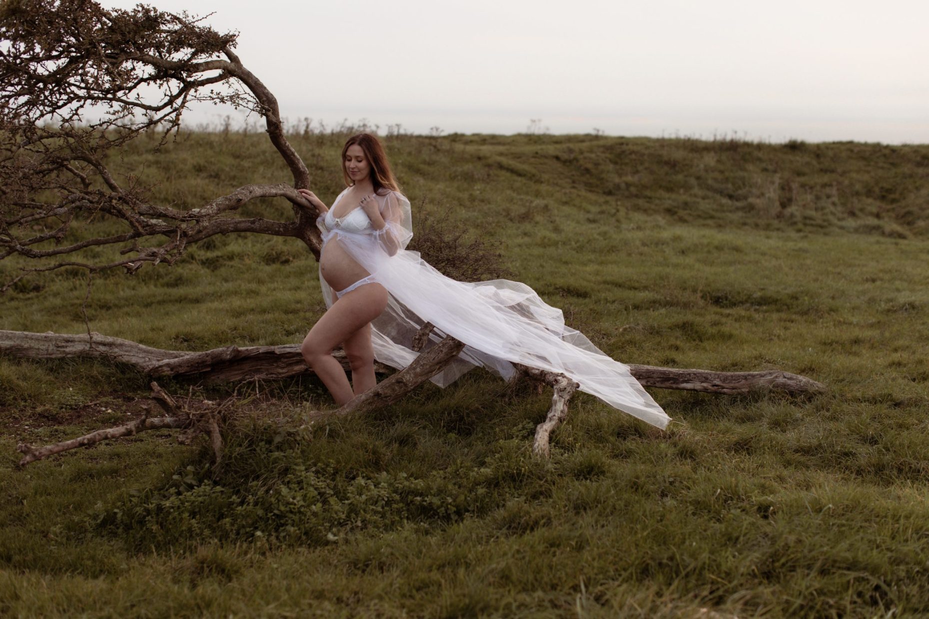 Beautiful pregnant woman stands in a flowing gown by a tree